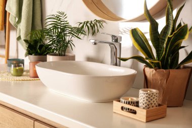 Lavabo tezgahı, mumlar ve beyaz mermer duvarın yanında güzel yeşil bitkiler.