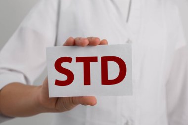 Beyaz arka planda STD kısaltması olan kağıt tutucu doktor, yakın plan.