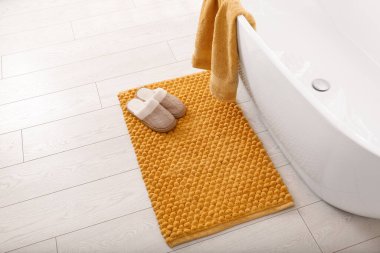 Yumuşak turuncu banyo paspası ve banyoda yerde terlikler.