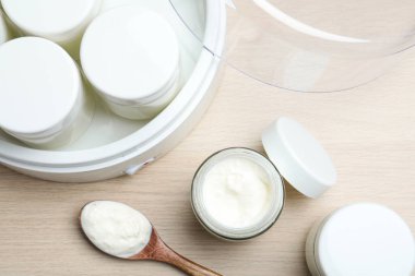 Modern yoğurt imalatçısı ve kavanozlar ahşap masada, düz yerde.