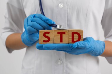 Doktor elinde kısaltması STD olan tahta küpler ve beyaz arka planda steteskop tutuyor.