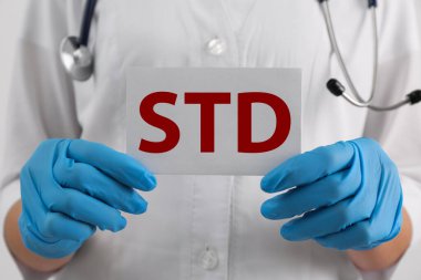 Beyaz arka planda STD kısaltması olan kağıt tutucu doktor, yakın plan.
