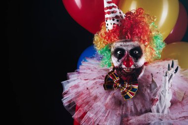 Siyah arka planda balonları olan korkunç bir palyaço, mesaj için yer var. Cadılar Bayramı partisi kostümü