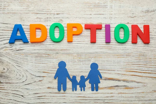 Beyaz ahşap masa üzerinde aile figürü ve kelime Evlat Edinme düz yatıyordu