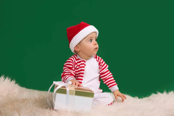 Niedliches Baby Weihnachtsmütze Mit Weihnachtsgeschenk Auf Flauschigem Teppich Vor Grünem — Stockfoto