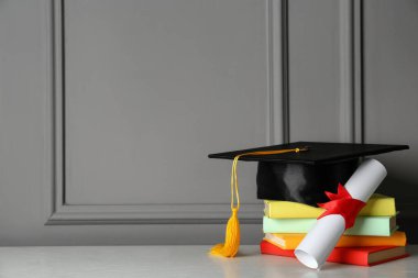Mezuniyet şapkası, kitaplar ve diploma gri duvarın yanındaki beyaz masada.