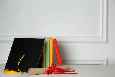 Mezuniyet şapkası, kitaplar ve diploma beyaz duvarın yanında, metin için yer var.
