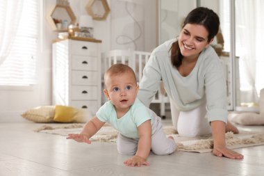 Mutlu genç anne, tatlı bebeğini evde yerde sürünürken seyrediyor.