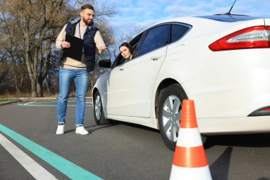Test pistinde genç bir bayanla arabanın yanında eğitmen. Sürücü kursu