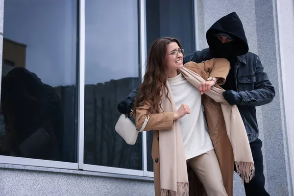 Woman fighting with thief while he trying to steal her bag near building, space for text. Self defense concept