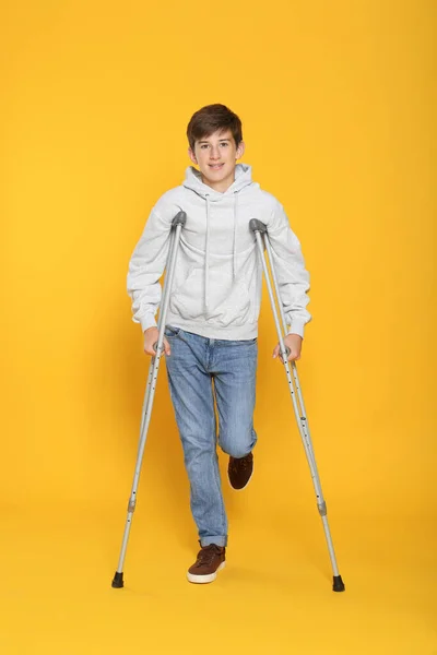 Adolescente Con Pierna Lesionada Usando Muletas Sobre Fondo Amarillo — Foto de Stock