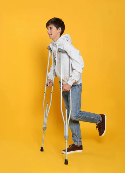 Adolescente Com Perna Ferida Usando Muletas Fundo Amarelo — Fotografia de Stock