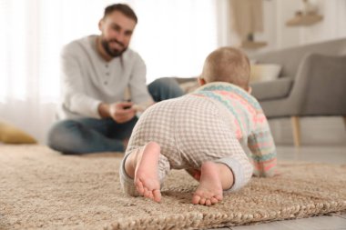 Mutlu genç baba, tatlı bebeğinin evde yerde sürünmesini izliyor.
