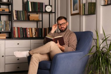 İçerideki koltukta kitap okuyan genç adam. Ev kitaplığı