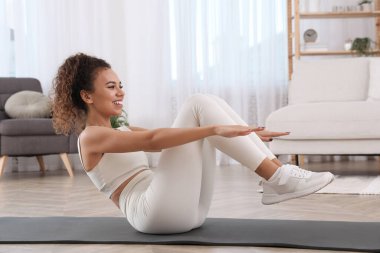 Güzel Afrikalı Amerikalı kadın evde yoga minderi üzerinde karın kası egzersizi yapıyor.