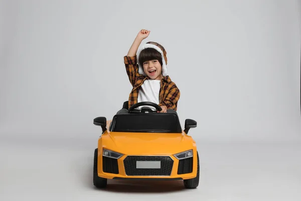 在灰色背景下驾驶儿童电动玩具车的戴飞行员帽的小男孩很可爱 — 图库照片