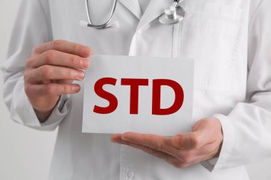 Beyaz arka planda STD kısaltması olan kağıt tutucu doktor, yakın plan.
