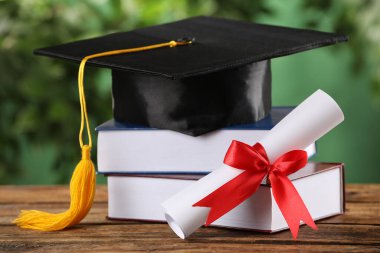 Mezuniyet şapkası, kitaplar ve diploma bulanık arka plana karşı ahşap masada.