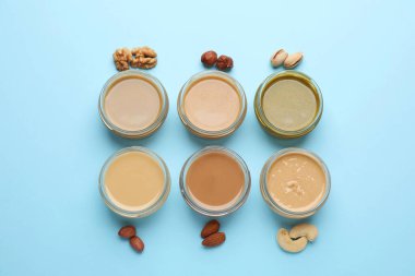 Farklı türde lezzetli fındık ezmesi ve açık mavi arka planda bulunan malzemeler.