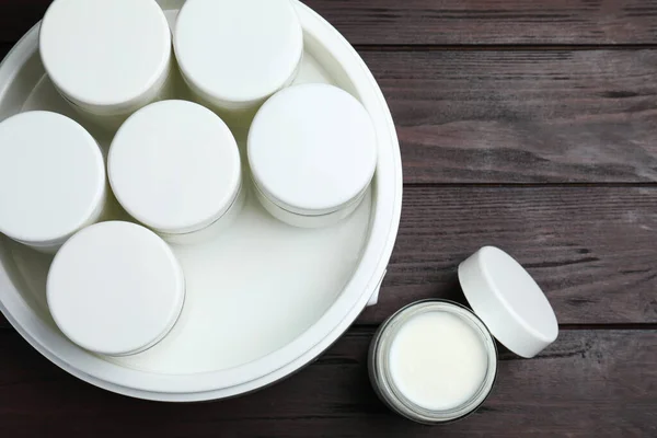 stock image Modern yogurt maker with full jars on wooden table, flat lay