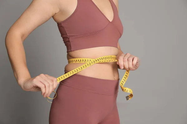 女性用灰色背景的带子测量腰围 — 图库照片