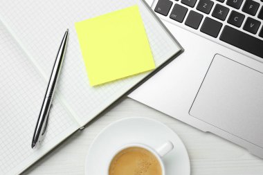 Laptop, boş yapışkan notlu defter, beyaz ahşap masa üzerinde bir fincan kahve ve kalem, düz yatak. Metin için boşluk