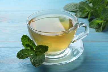 Açık mavi ahşap masada sıcak aromalı nane çayı.