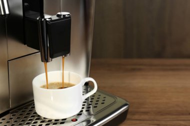 Modern espresso makinesi kahveyi ahşap masaya koyuyor, yakın plan. Metin için boşluk