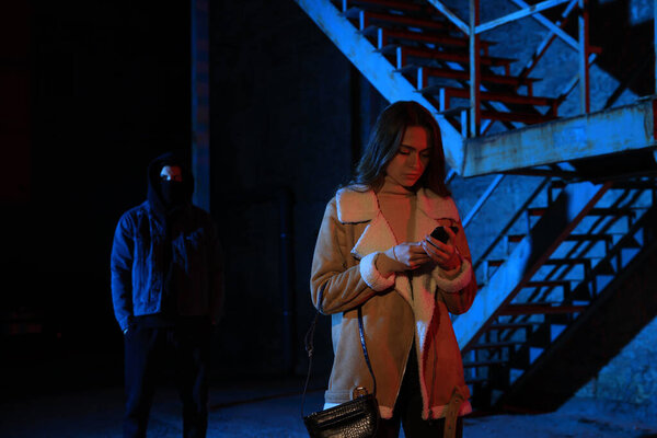 Man in mask stalking young woman outdoors at night