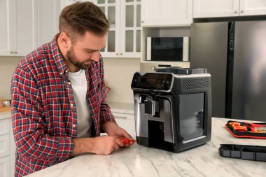 Mutfaktaki masada kahve makinesini tamir eden tornavidalı bir adam.