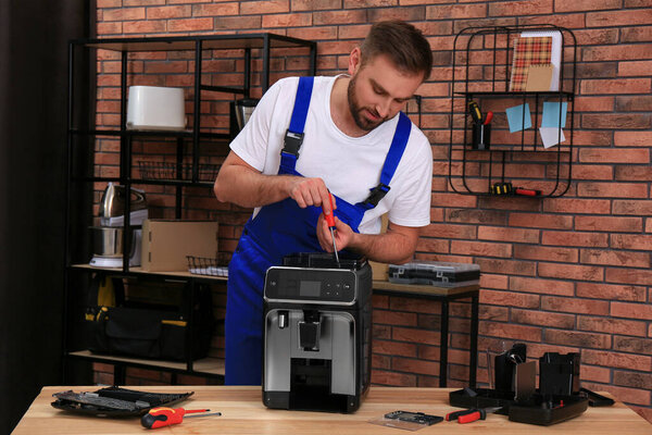 Repairman with screwdriver fixing coffee machine at table indoors
