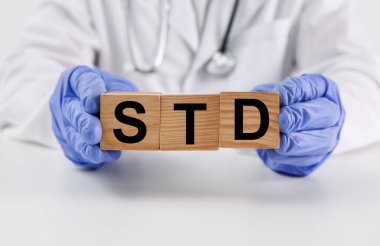 Doktor elinde tahta küplerle beyaz masada STD kısaltması tutuyor.