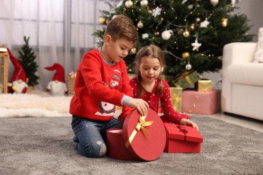 Evde Noel ağacının yanında hediye kutuları olan şirin çocuklar.