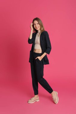 Pembe arka planda şık takım elbiseli güzel bir genç kadının tam boy portresi. İş kıyafeti