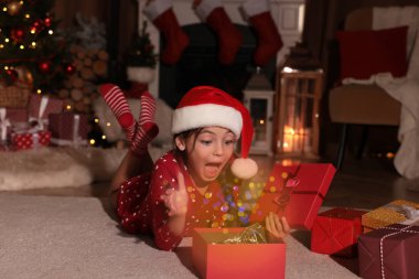 Noel şapkalı süpriz çocuk evde yerde Noel hediyesini açıyor.