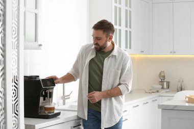 Genç adam mutfakta modern makineyle taze aromatik kahve hazırlıyor.