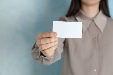 Açık mavi arka planda boş kartviziti olan bir kadın, yakın plan. Tasarım için model