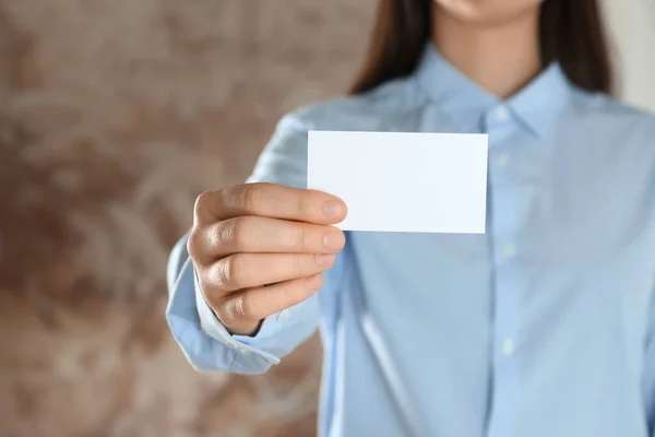Woman holding blank business card on blurred background, closeup. Mockup for design