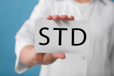 Açık mavi zemin üzerinde STD kısaltması olan kağıt tutucu doktor, yakın plan.