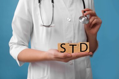 Doktor elinde tahta küplerle açık mavi arka planda STD kısaltması var.