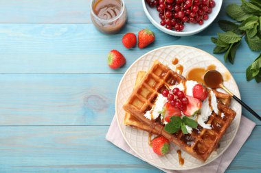 Turkuaz ahşap masada servis edilen böğürtlen ve karamel soslu leziz Belçika waffleları. Metin için boşluk
