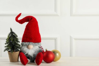 Şirin Noel cücesi, küçük dekoratif köknar ağacı ve beyaz ahşap masada şenlikli toplar. Metin için boşluk
