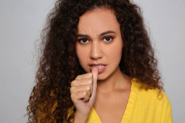 Gri arka planda tırnaklarını yiyen Afro-Amerikalı kadın.