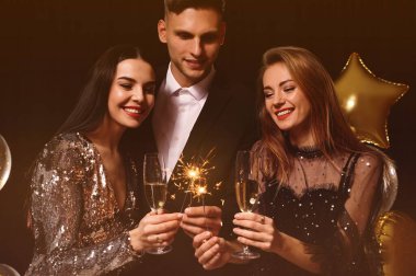 Köpüklü şarap ve maytap kadehleriyle mutlu arkadaşlar siyah arka planda yeni yılı kutluyorlar.