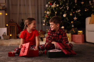 Evde Noel ağacının yanında hediye kutuları olan şirin çocuklar.