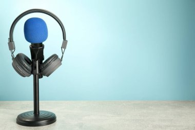 Açık mavi arkaplan, metin için alan, gri masadaki mikrofon ve modern kulaklıklar