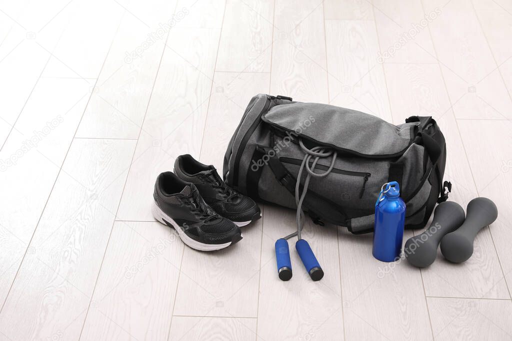 Sports bag and gym equipment on white floor. Space for text