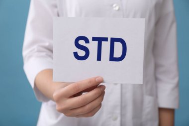 Açık mavi zemin üzerinde STD kısaltması olan kağıt tutucu doktor, yakın plan.