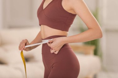Spor kıyafetli bir kadın, evde bantla ölçü alıyor, yakın plan.