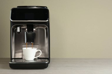 Modern espresso makinesi bej duvarın yanındaki ahşap masaya kahve dolduruyor. Metin için boşluk